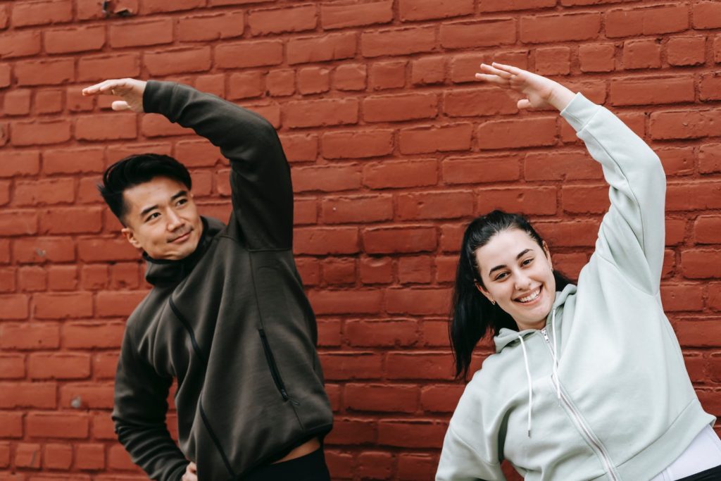 Musculation alcool week-end, quel est son impact sur tes résultats ? 11 Positive young obese woman and Asian male trainer in sportswear warming up before outdoor training standing near brick wall