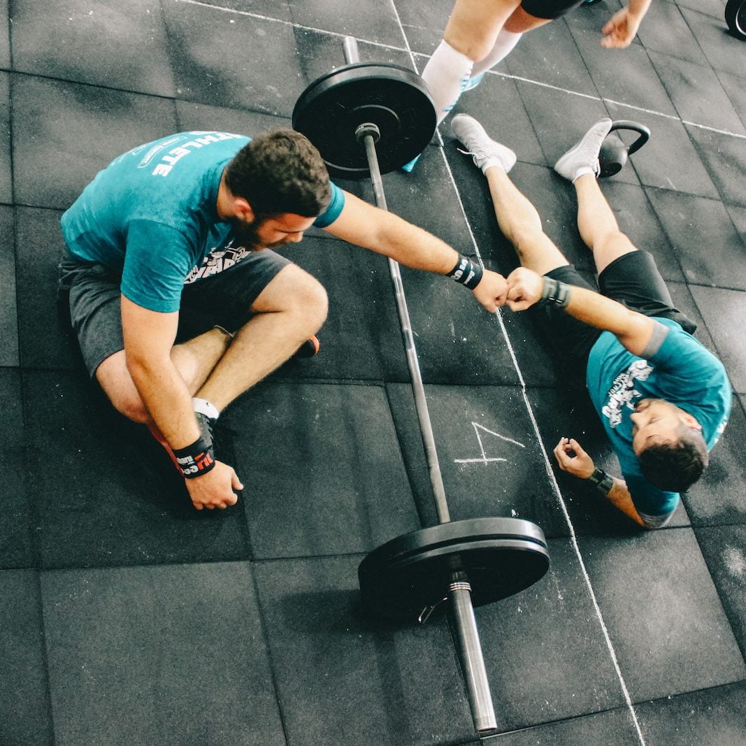Le Crossfit, qu’est-ce que c’est ? 1 man fist bump to man laying on ground after a Crossfit session