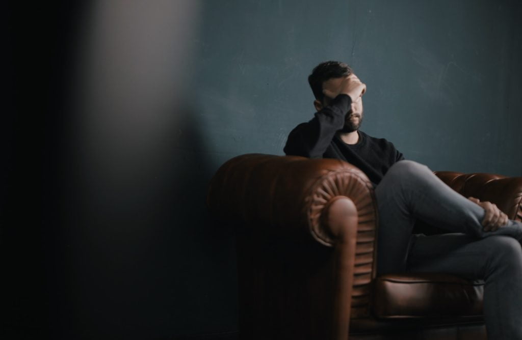 Surentraînement musculation et sport 11 a man holds his head while sitting on a sofa